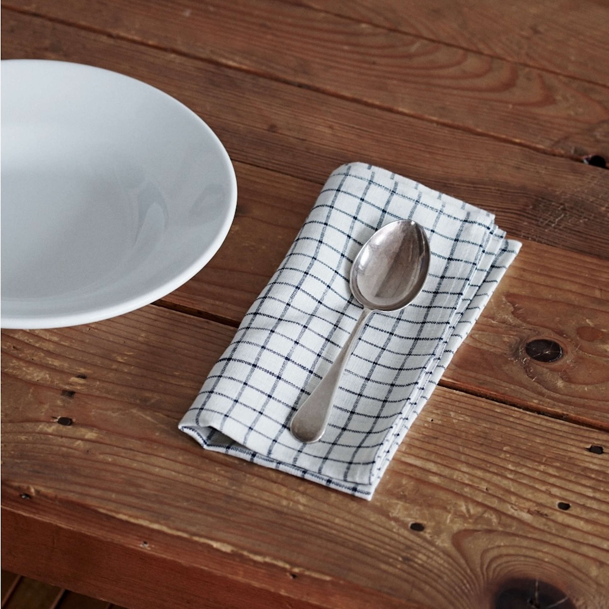 Spoon on a checkered cloth with a white bowl on a wooden surface