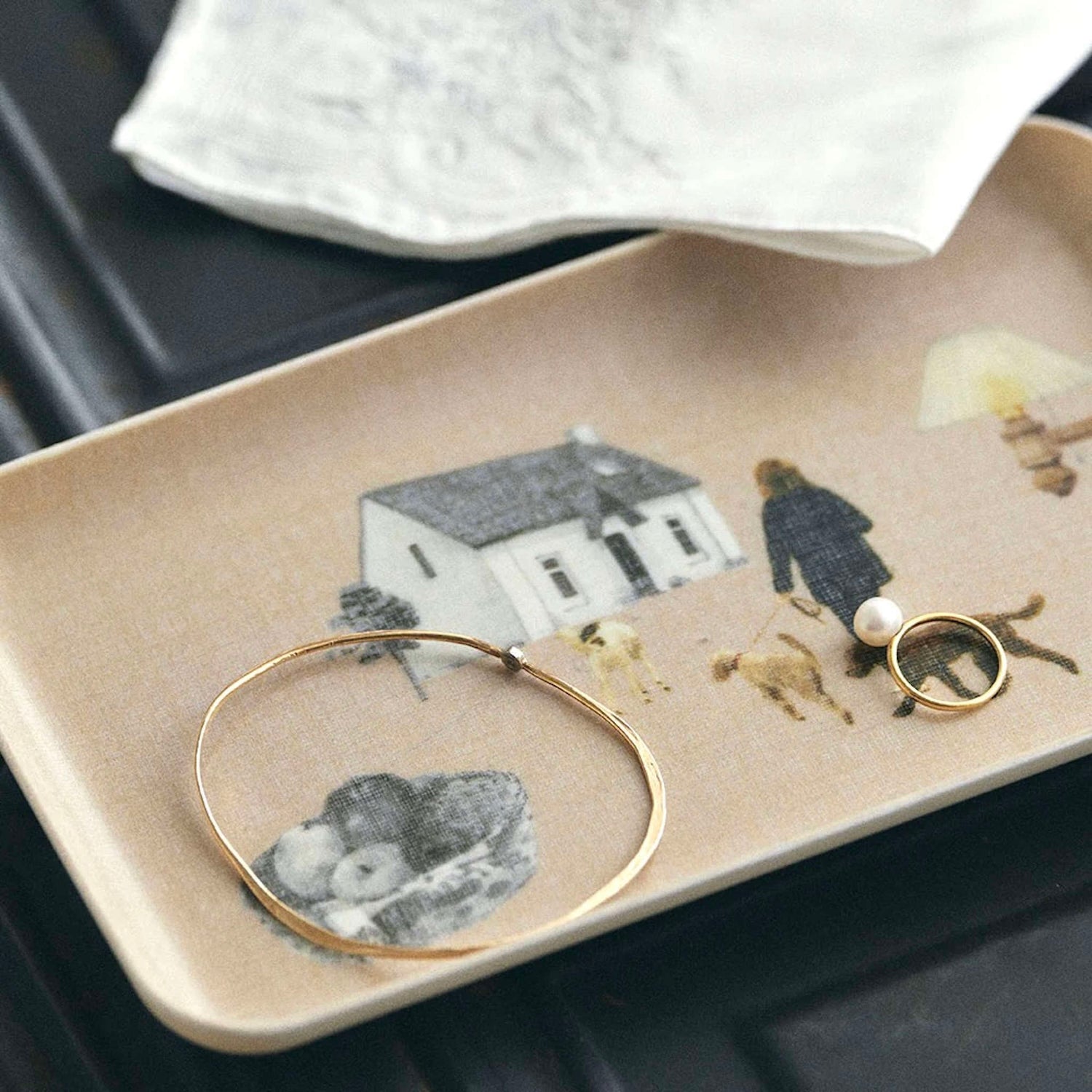 Jewelry on a decorative tray with illustrations of a house, people, and dogs.