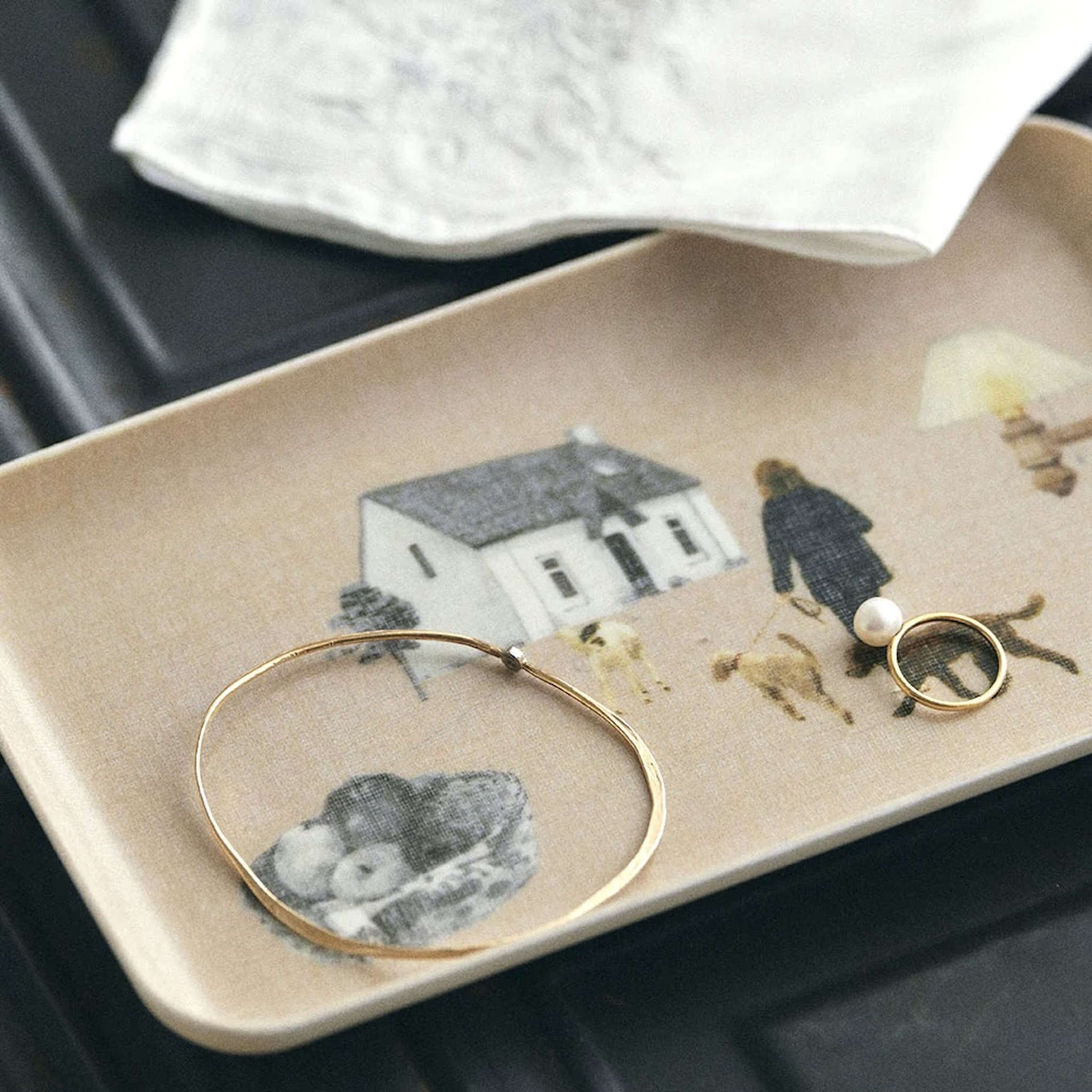 Jewelry on a decorative tray with illustrations of a house, people, and dogs.