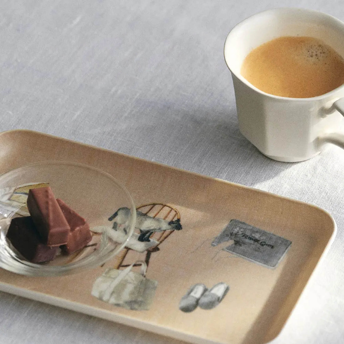 Linen coated tray with chocolate bar next to a cup of coffee on a light gray surface.