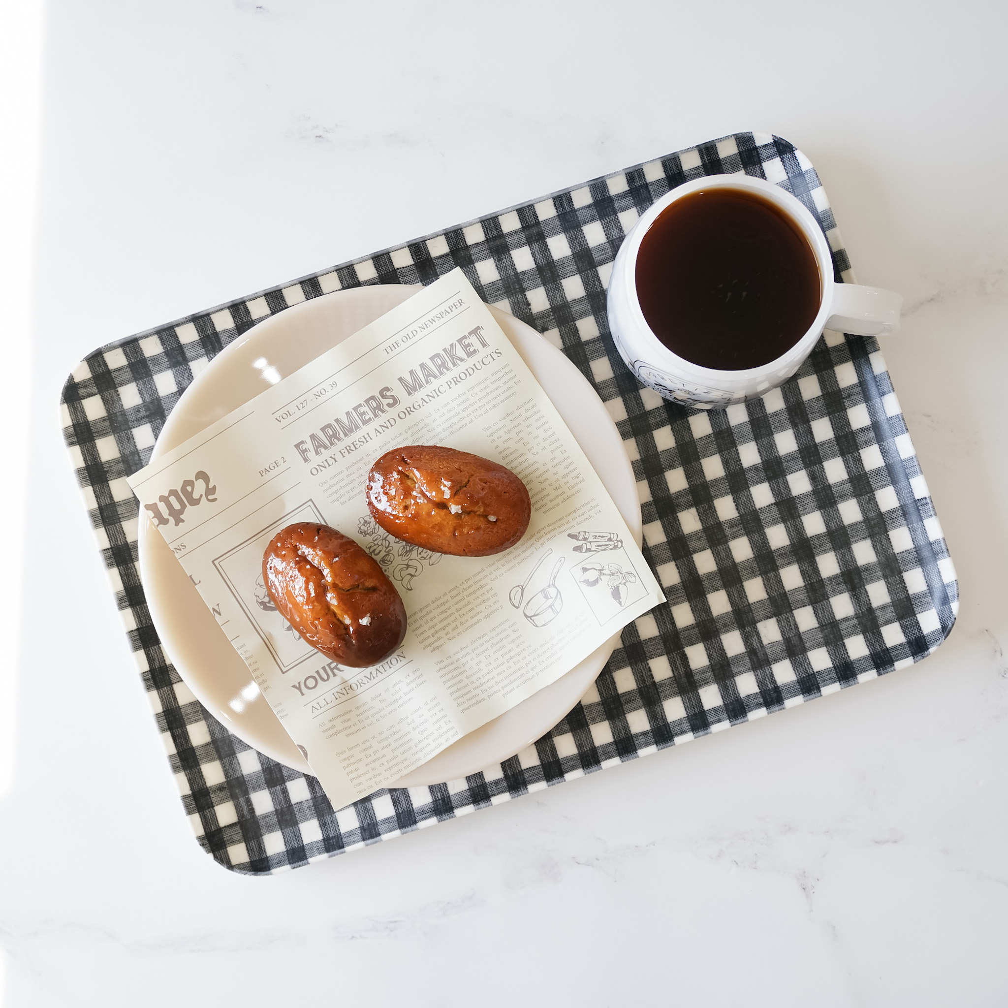 A dark navy check linen coated tray with a cup of coffee and two pastries on a plate, placed on a white surface.