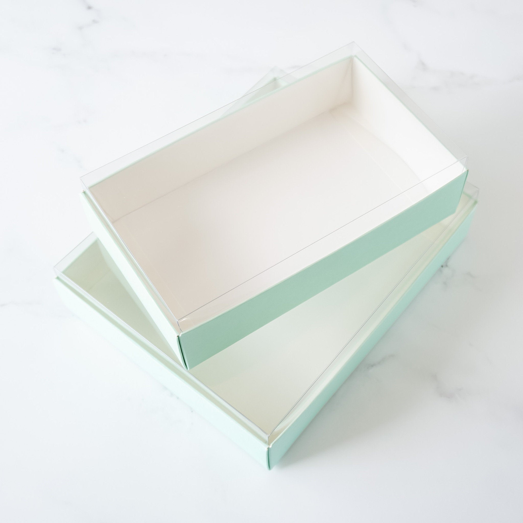 Two light green rectangular boxes with clear plastic lids. The boxes are stacked on top of each other.