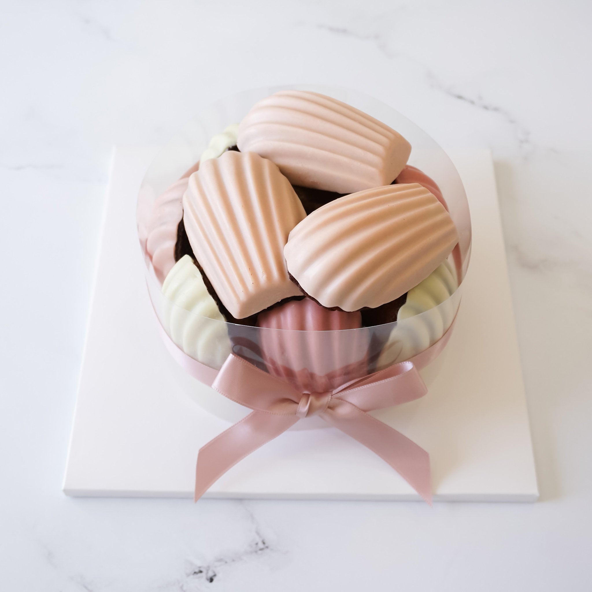 A madeleine cake presented on a white square cake board with a matte finish.