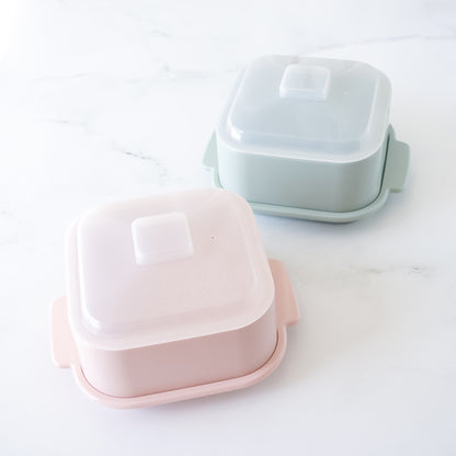 Two rectangular microwave steamer with lids, one pink and one light blue, on a white surface.