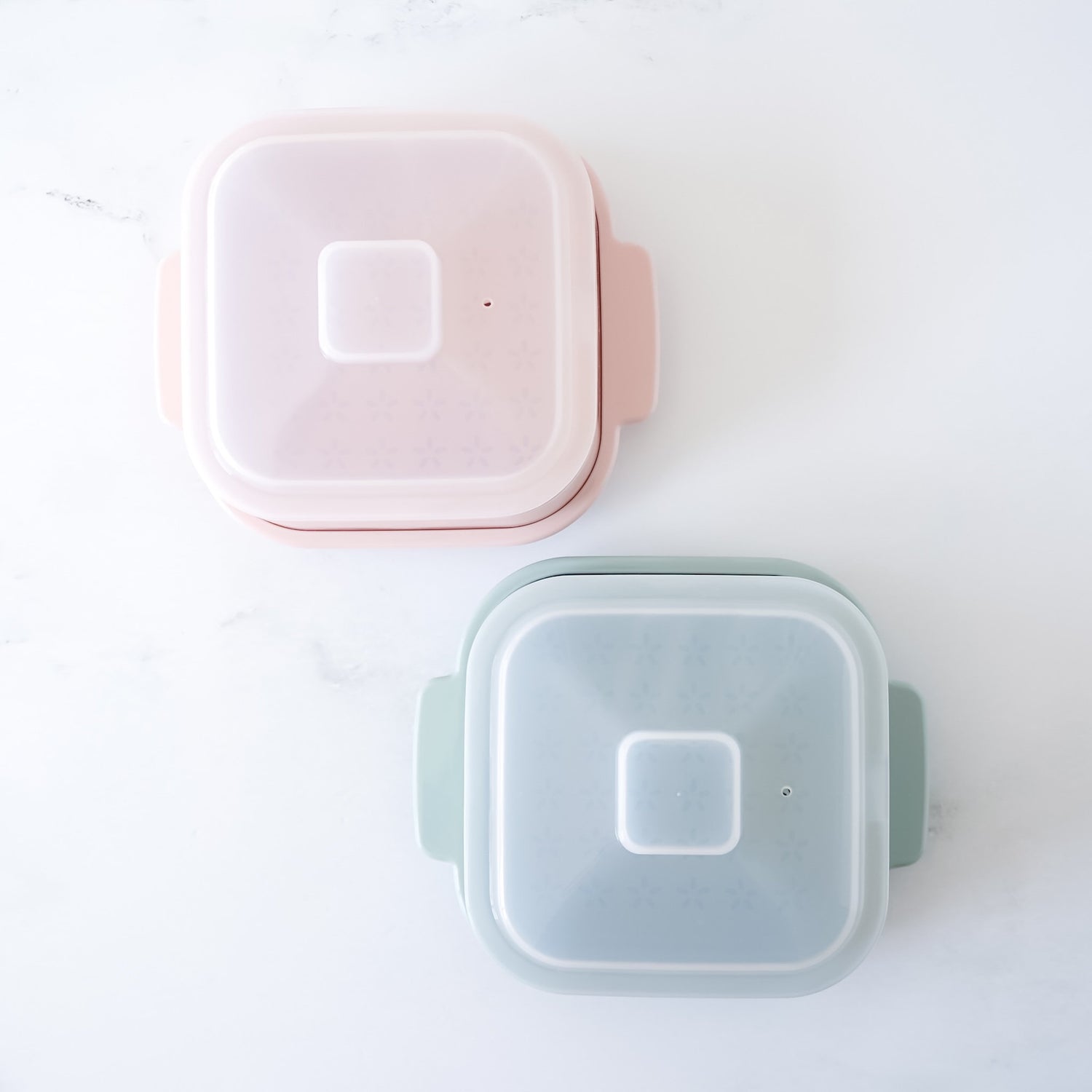 Two square steamer containers, one pink and one green, on a white background.