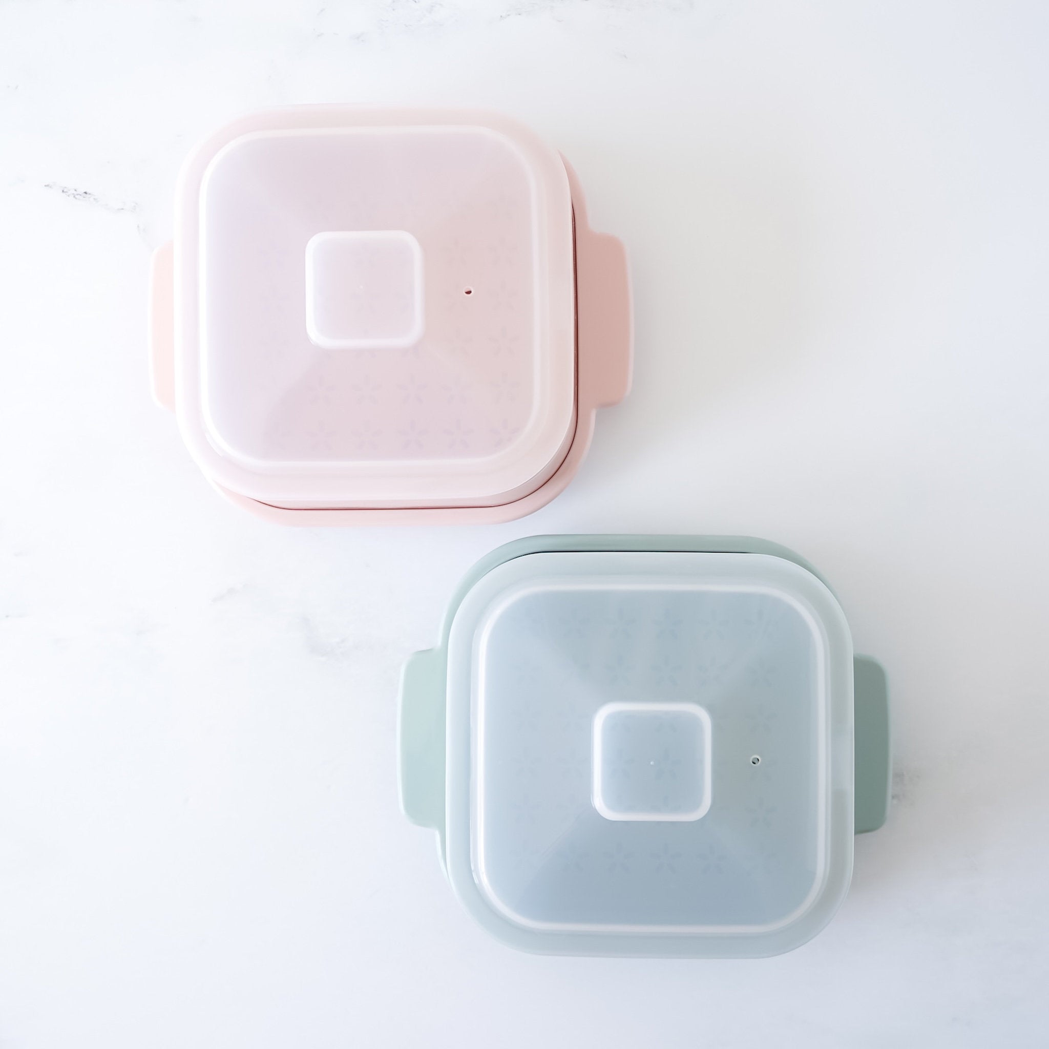 Two square steamer containers, one pink and one green, on a white background.
