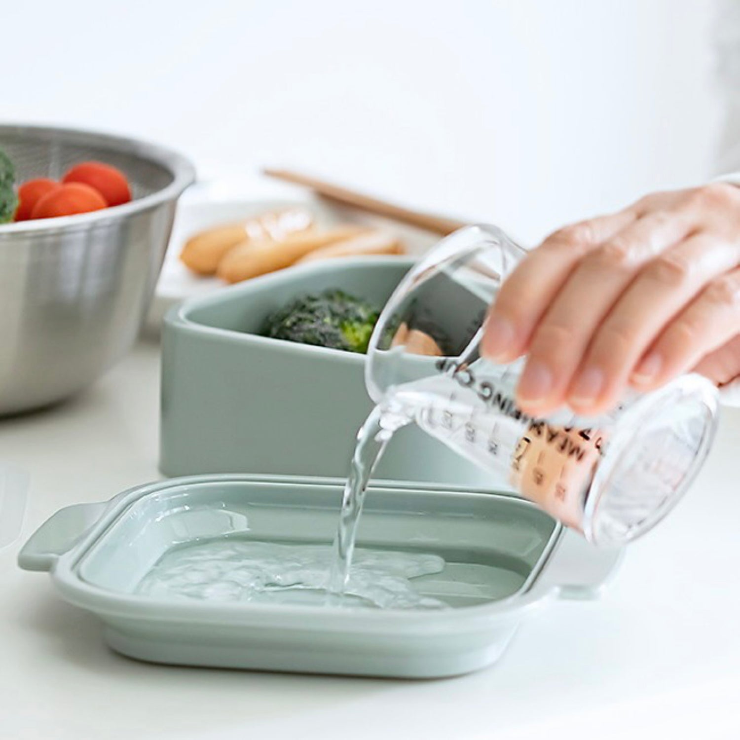 Person pouring water into a green steamer dish on a kitchen counter.
