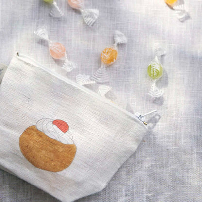 White pouch with a dessert design on a textured surface with candies around