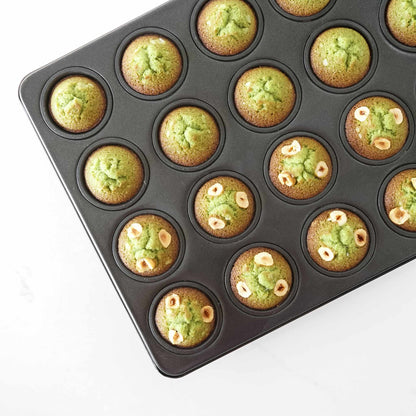 Mini muffin tray with green muffins on a white background