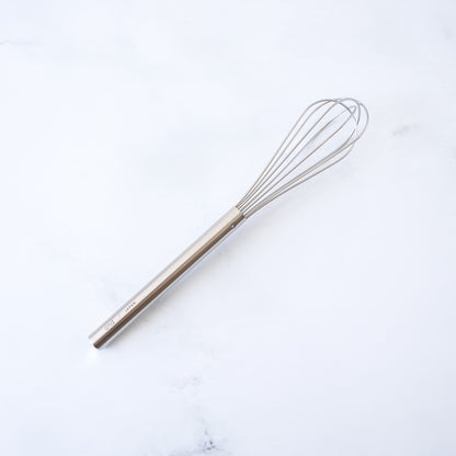 Stainless steel mini whisk on a white marble surface