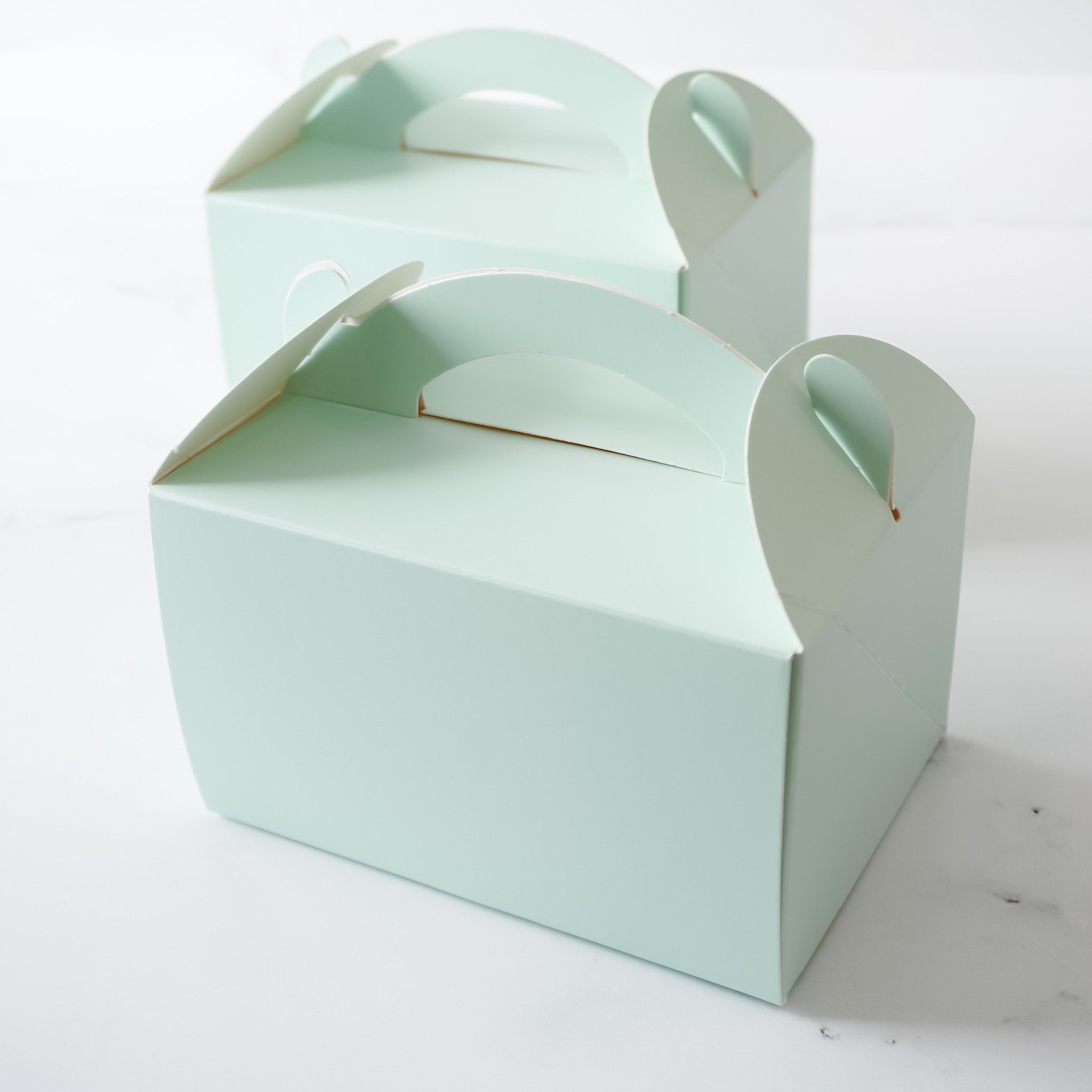 Two light green cardboard boxes with cut-out handles. The boxes are empty and have a smooth surface.