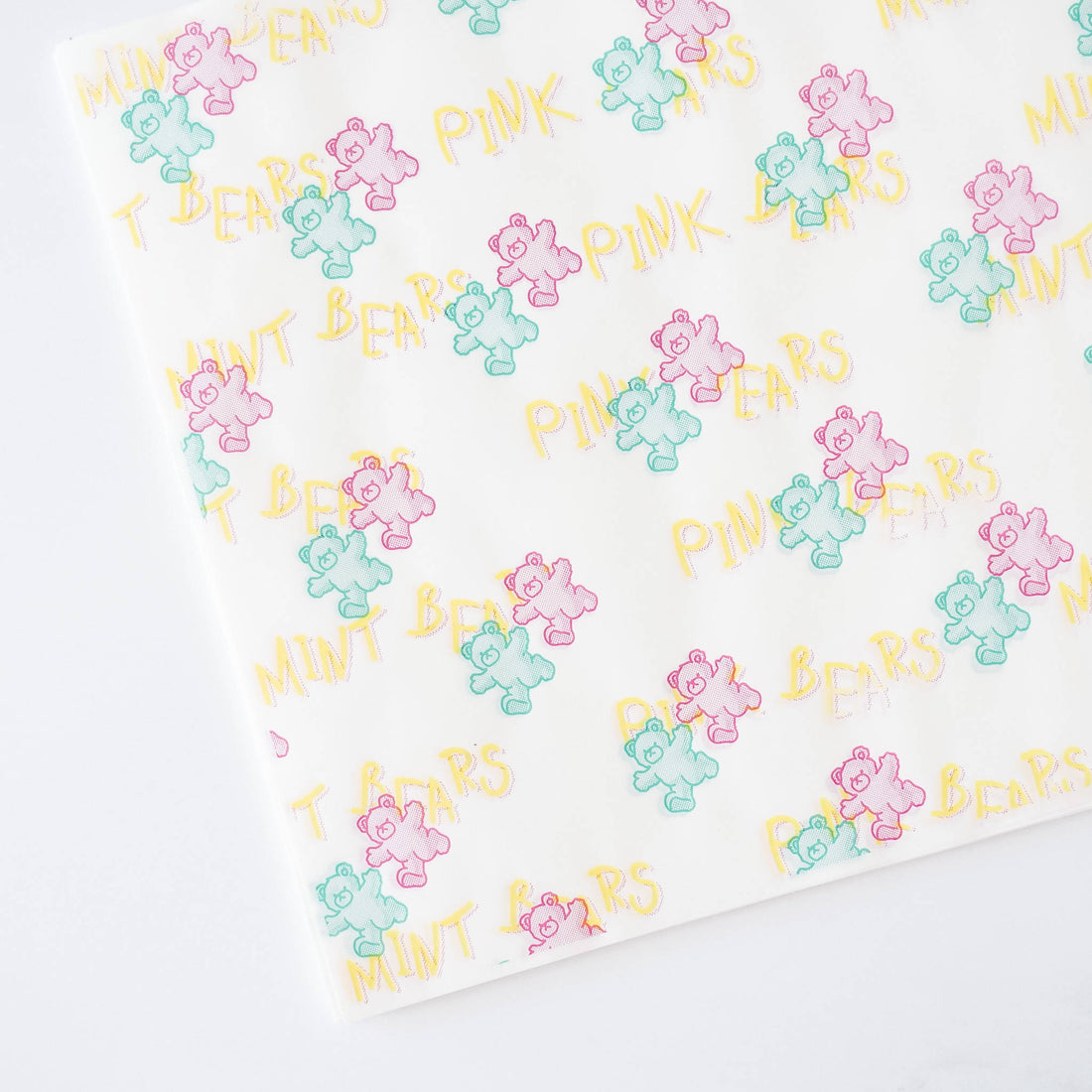 White food wrapping paper with a repeating pattern of pink, green, and blue cartoon bears. The text &