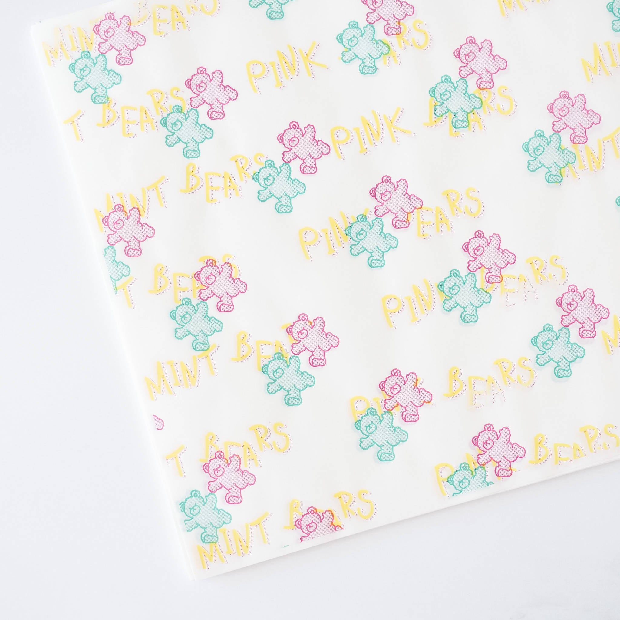 White food wrapping paper with a repeating pattern of pink, green, and blue cartoon bears. The text &