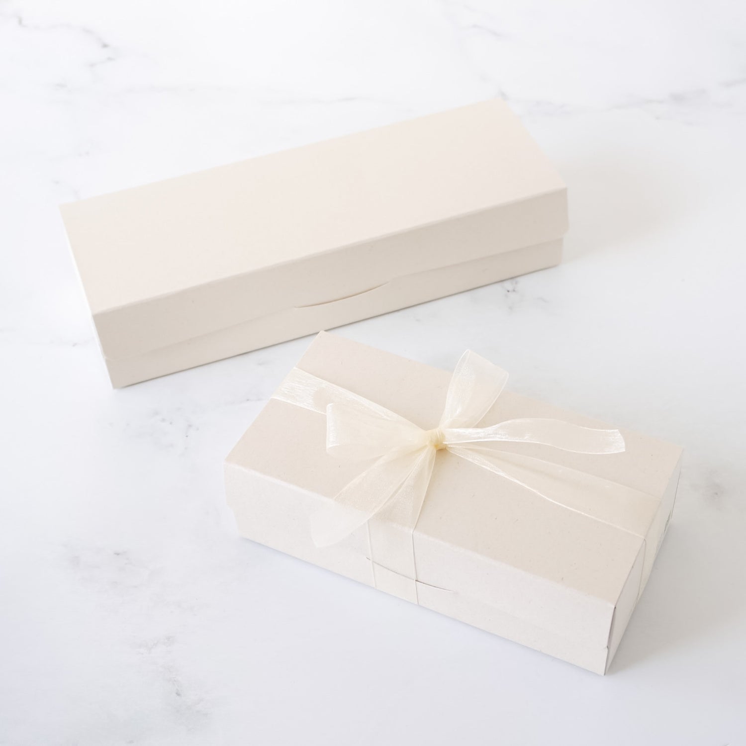 Two beige gift boxes with ribbons on a white surface