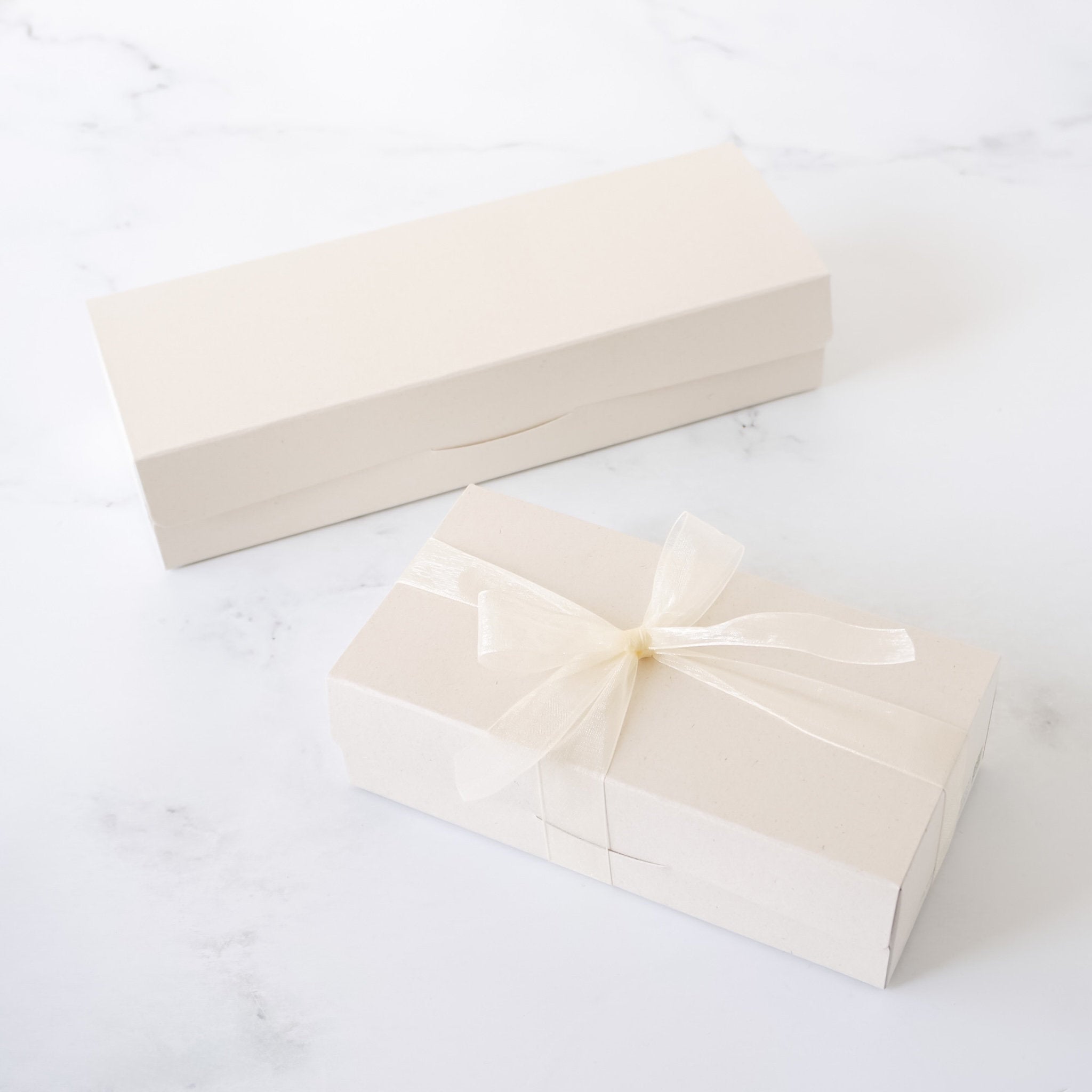Two beige gift boxes with ribbons on a white surface