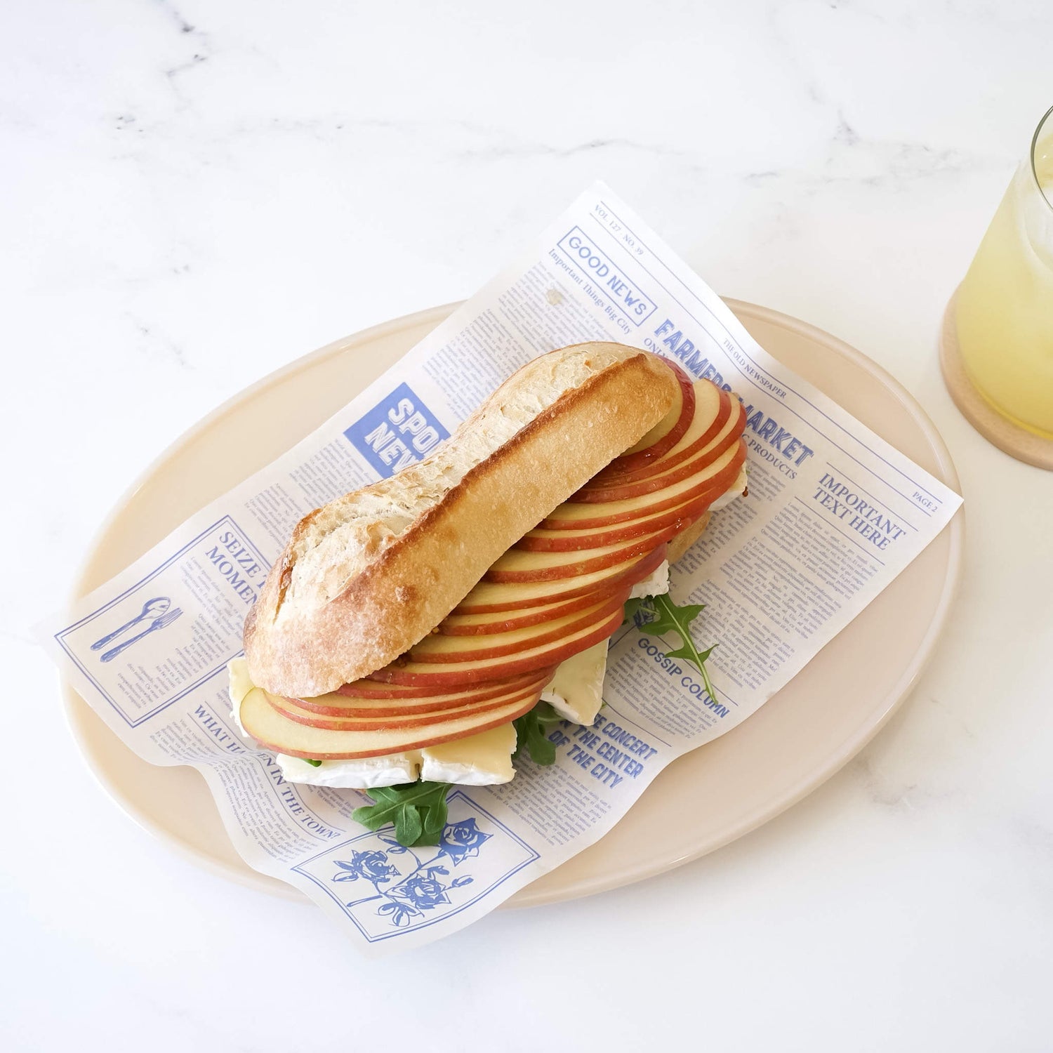 apple brie cheese sandwich on newspaper printed deli paper in blue