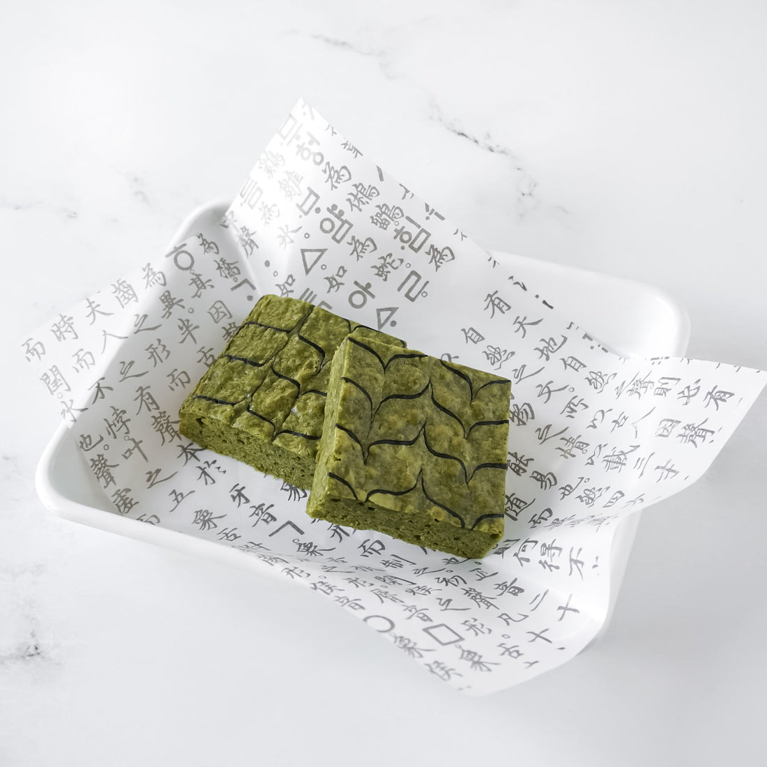 Two matcha brownies on a white plate with original hangul Korean text