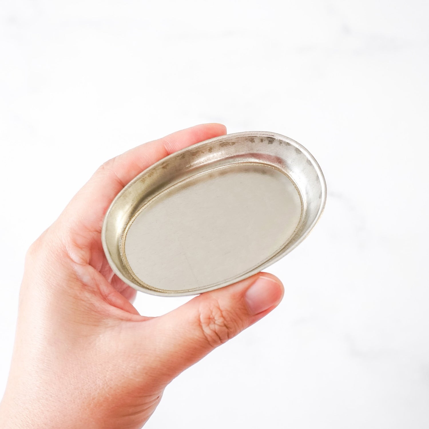 Hand holding a metallic oval financier pan against a white background