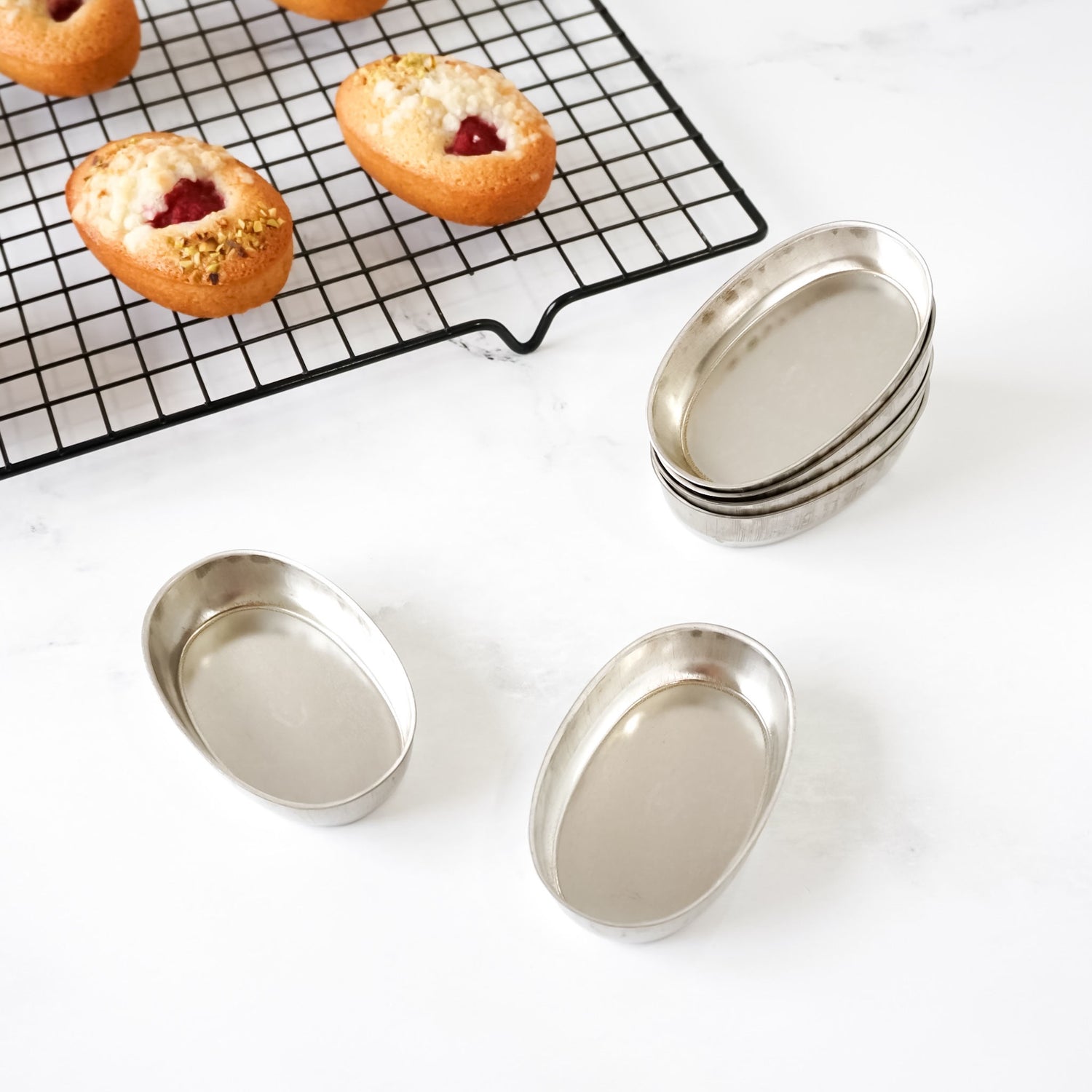 Metal baking pans on a white surface with pastries on a cooling rack in the background.