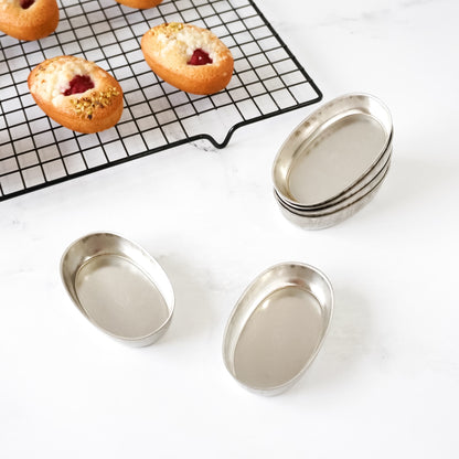 Metal baking pans on a white surface with pastries on a cooling rack in the background.