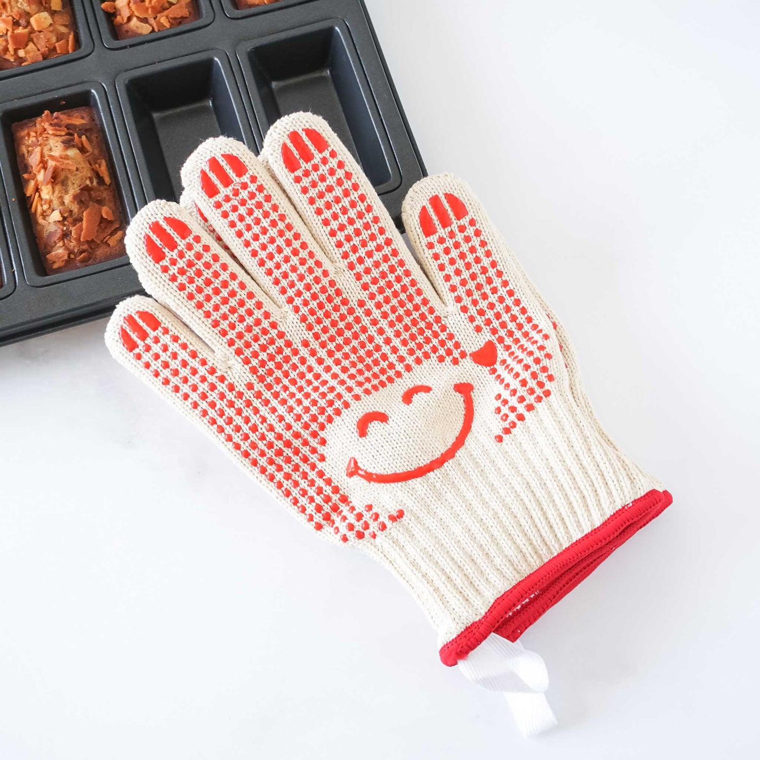 White oven mitt with red textured grip and smiley face design on a white background