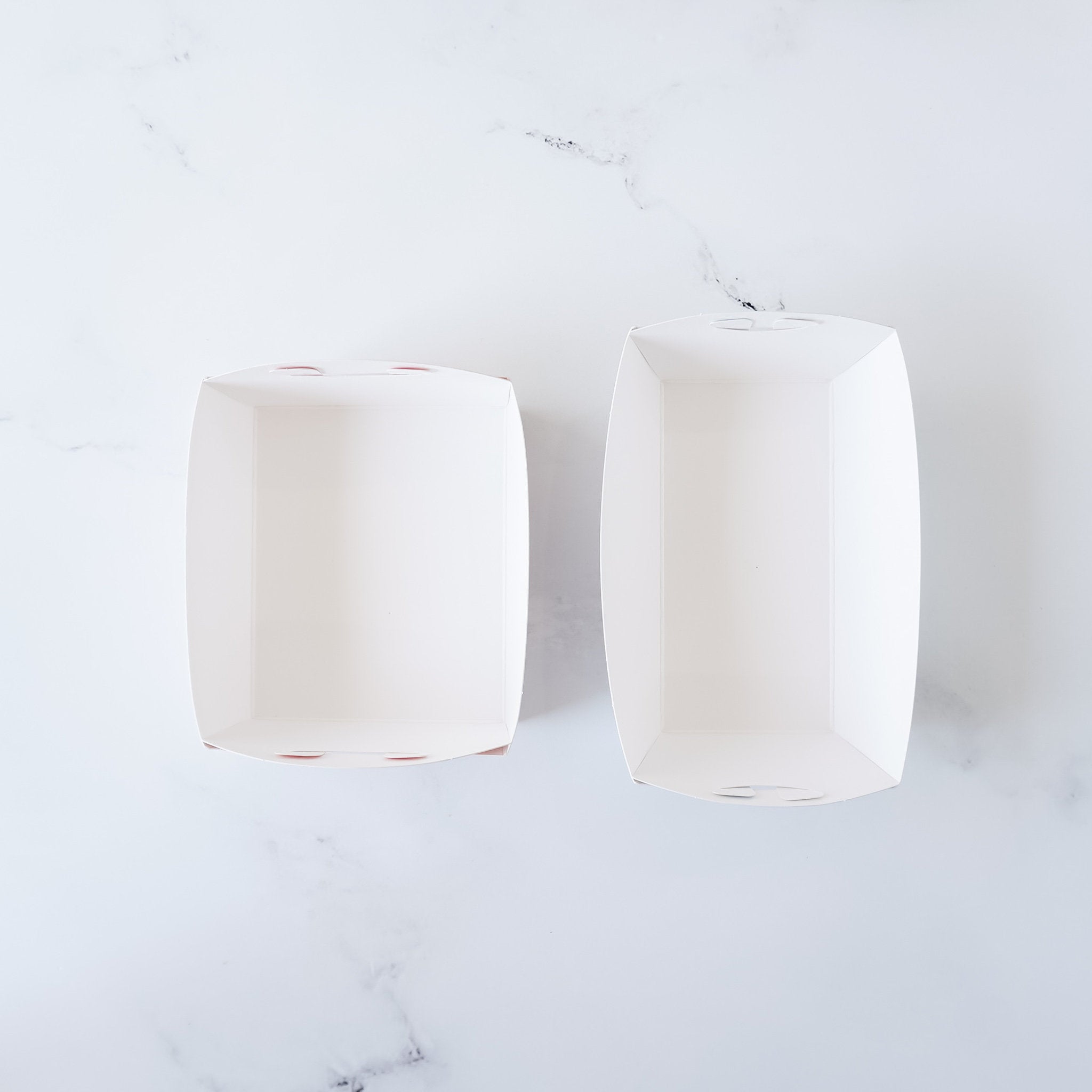 Two empty white paper food containers with a dotted pattern on the bottom. The containers are on a white marble surface.