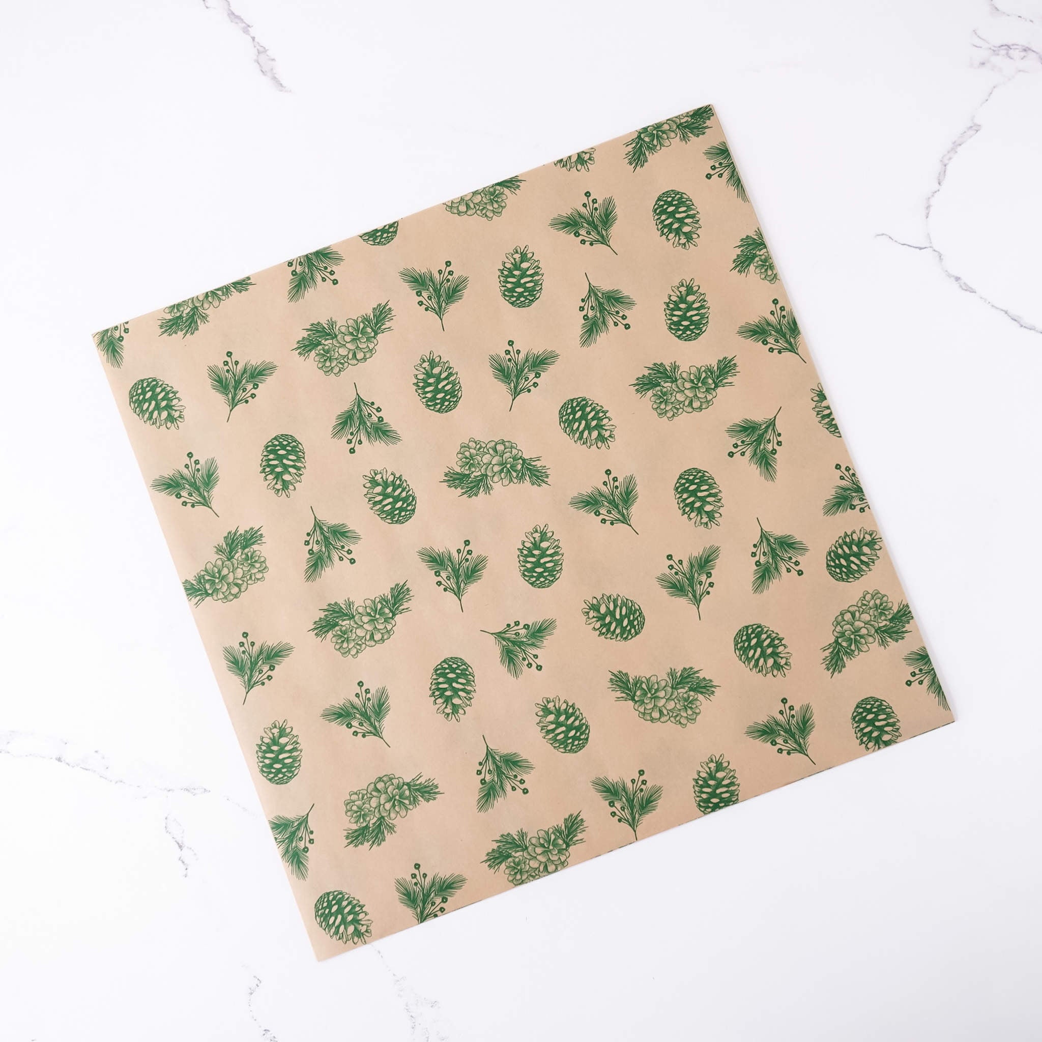 Beige paper with green pine cone pattern on a white marble background
