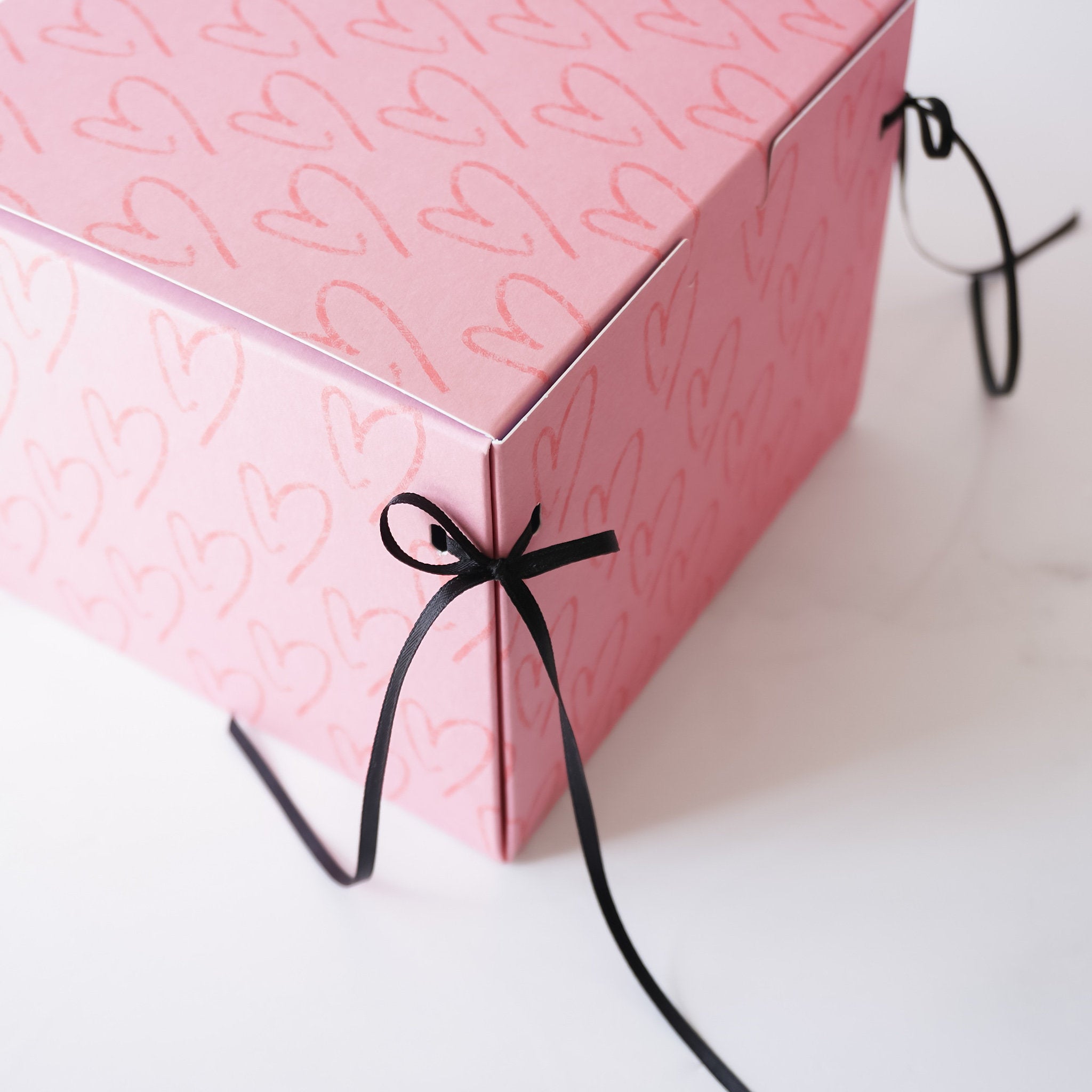 A pink gift box with a heart pattern and black ribbon tied in a bow
