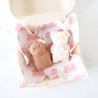 Two bear-shaped madeleines with flowers on a pink patterned deli paper.