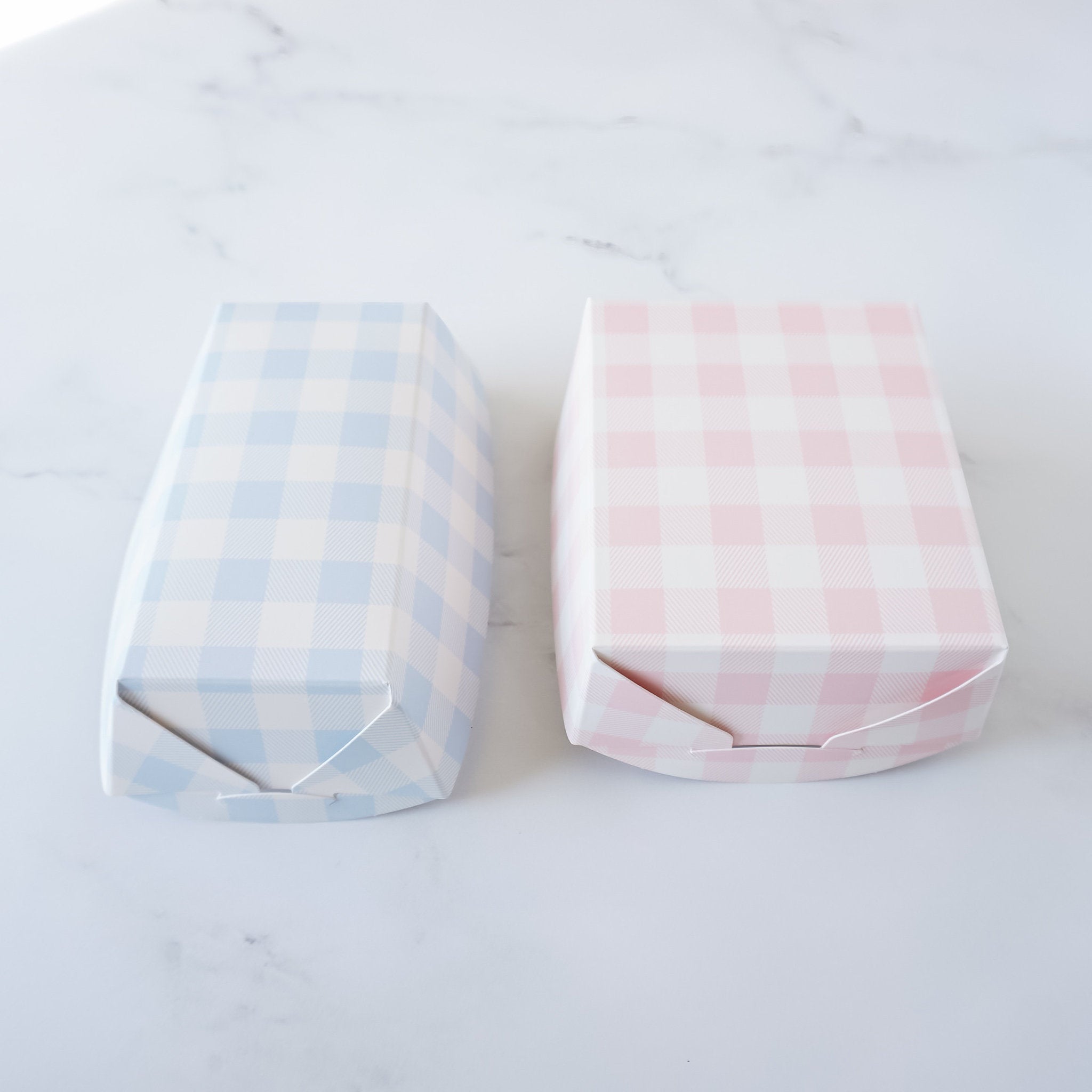 Two small, empty, paper trays with a gingham pattern. One box is blue and white gingham and the other is pink and white gingham.