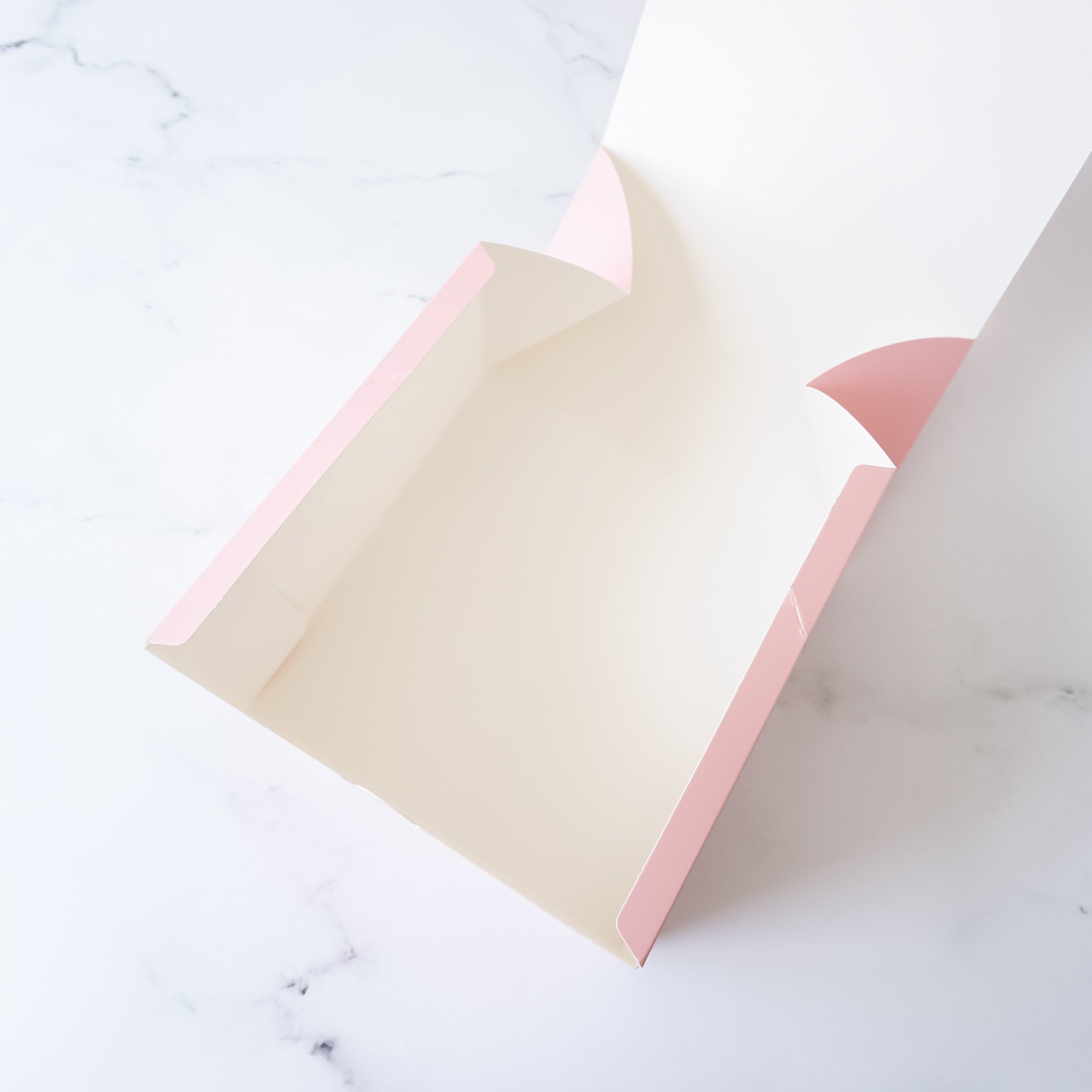 A pink cardboard box with a white interior. The box is open and the inside is visible. The box is on a white marble surface.