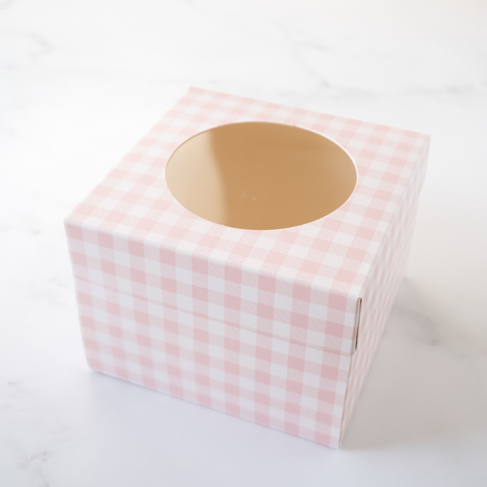 A pink and white gingham gift box with a round window in the top. The box is empty.
