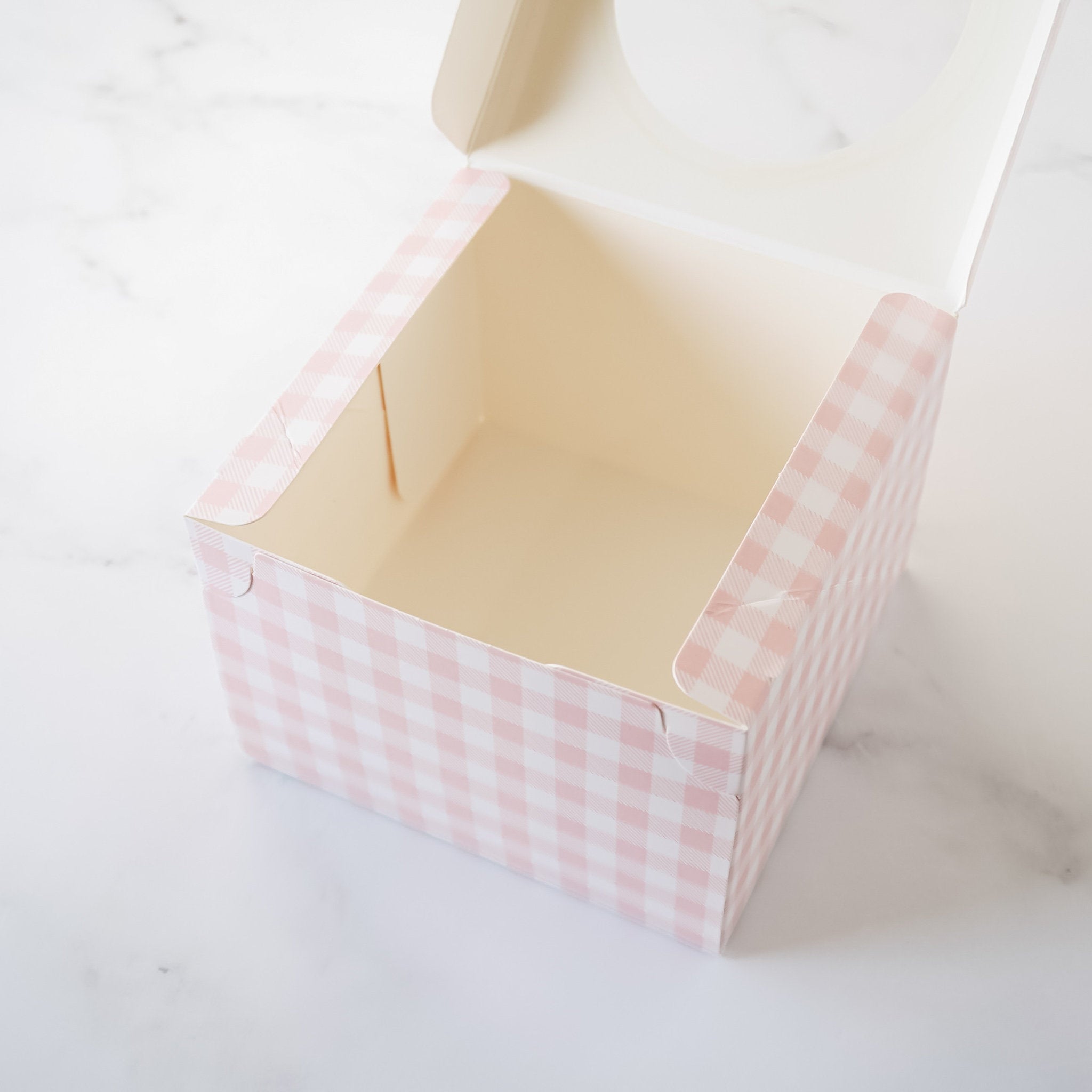 An empty pink and white gingham patterned cardboard box with a window on the top.