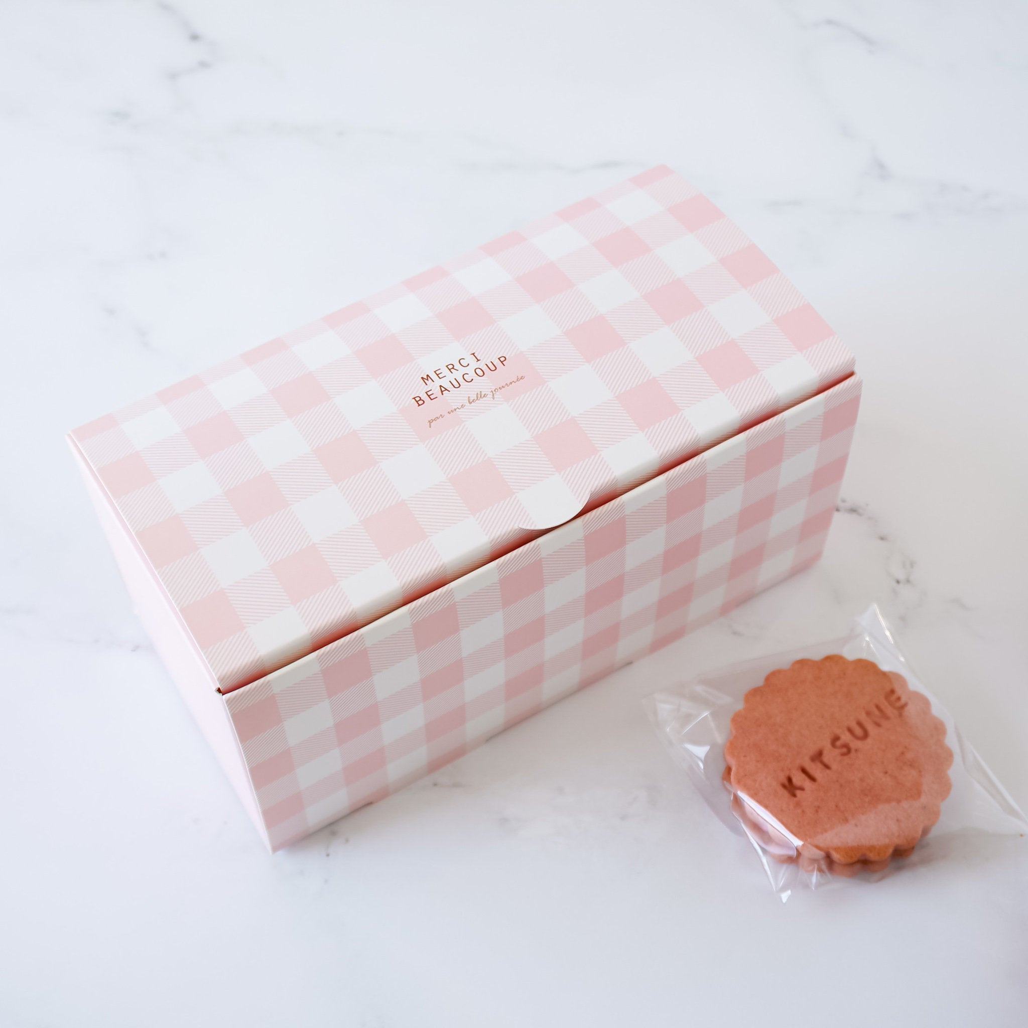 A pink gingham patterned cookie box with the text &