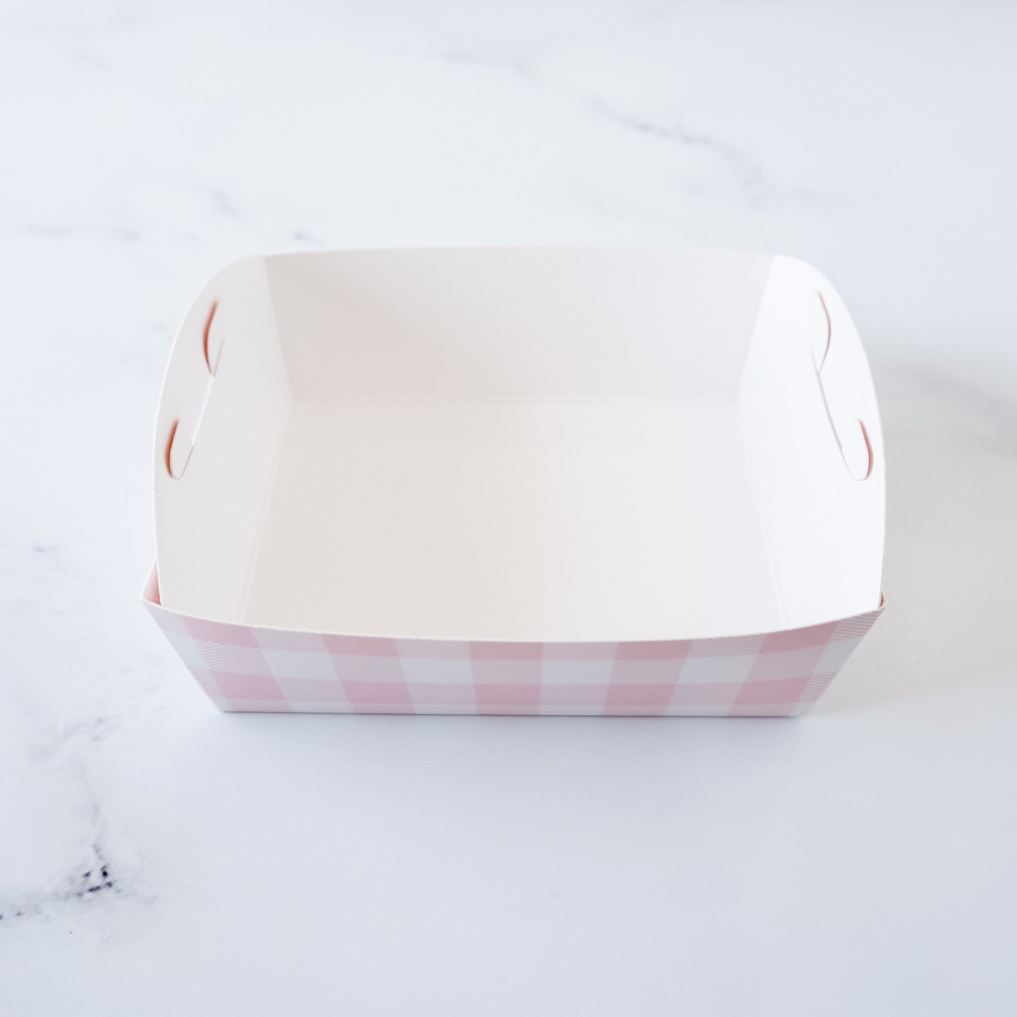 A white paper food tray with pink and white checkered pattern on the bottom. The tray has two small cut-out handles on each side.