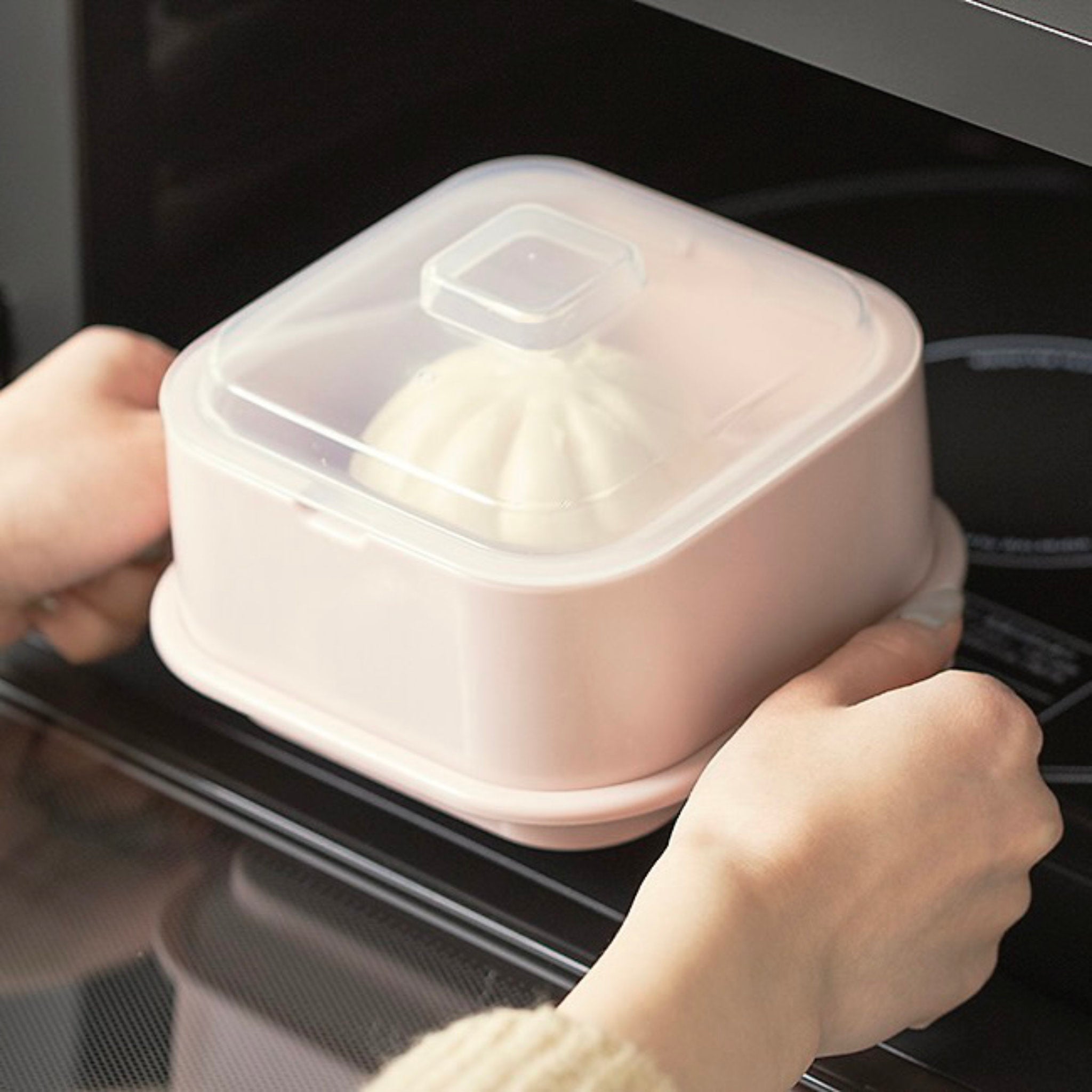 Person holding a pink container with a lid over a microwave.