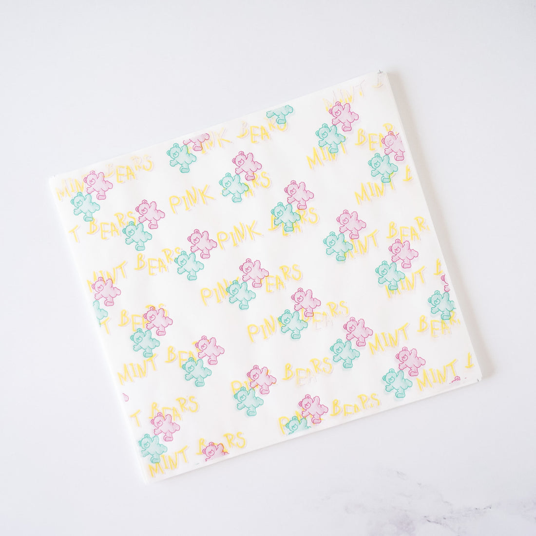A sheet of deli paper with a pattern of pink and mint colored bears on a white background, placed on a white surface.