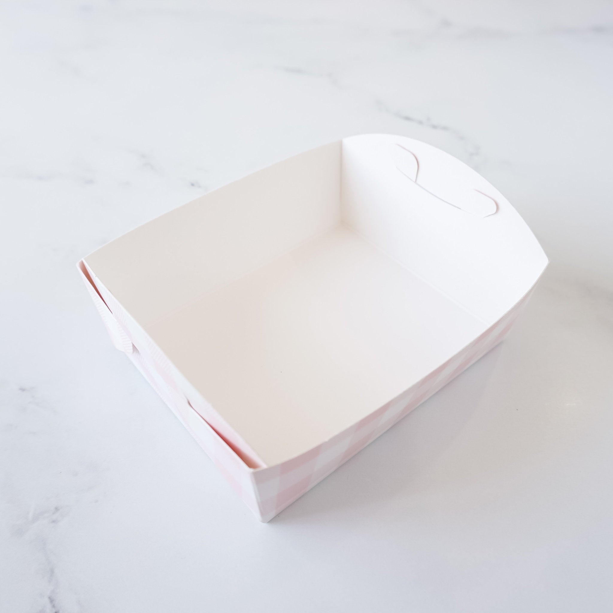 A white paper food container with a pink and white checkered pattern. The container has a handle on the top and is empty.