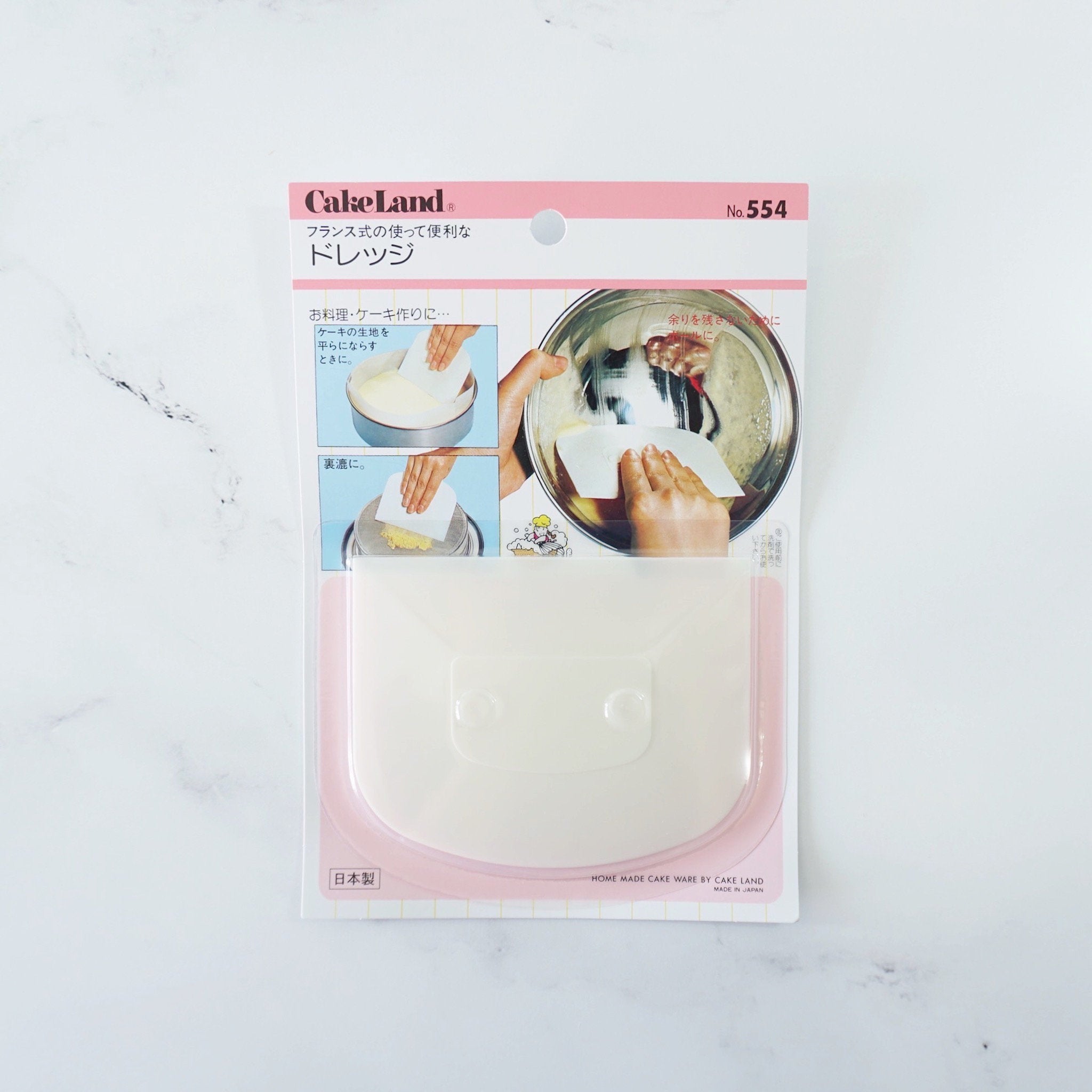 A packaged plastic cake scraper with a pink and white design, displayed against a white background.