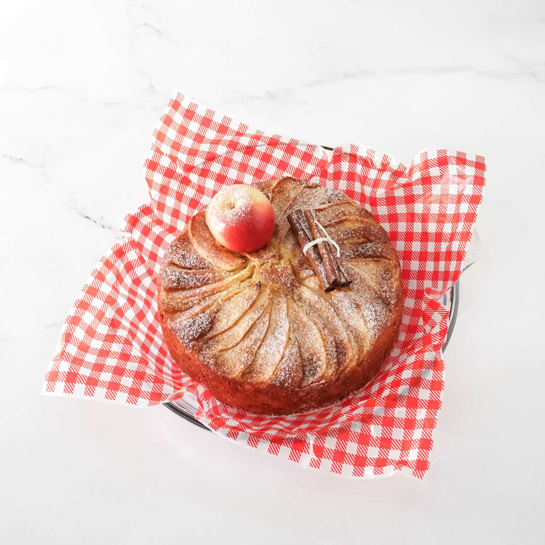 Baked apple cake with a cinnamon stick on a red and white checkered deli paper