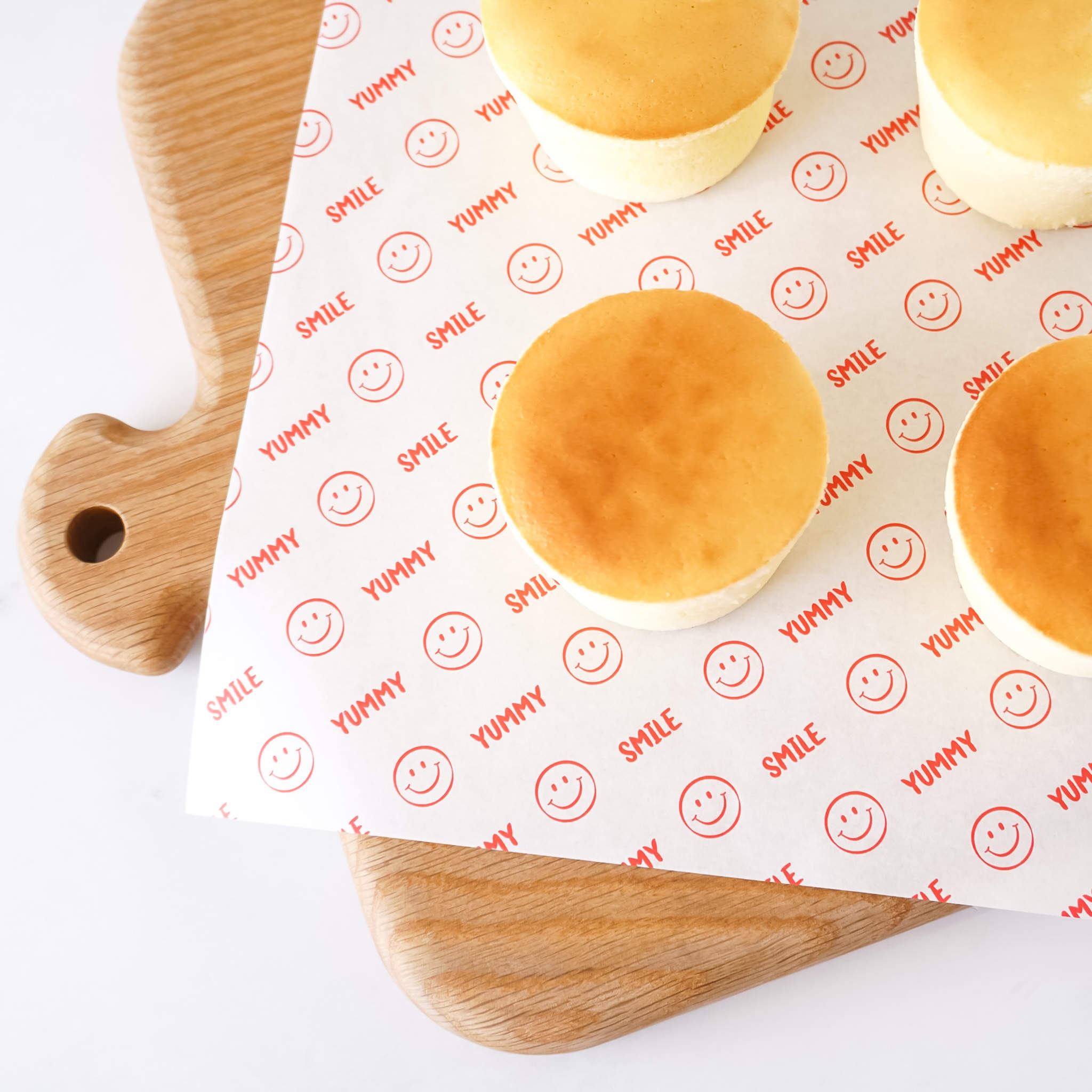 Baked goods on a sheet of deli paper with smiley face patterns and text, placed on a wooden cutting board.