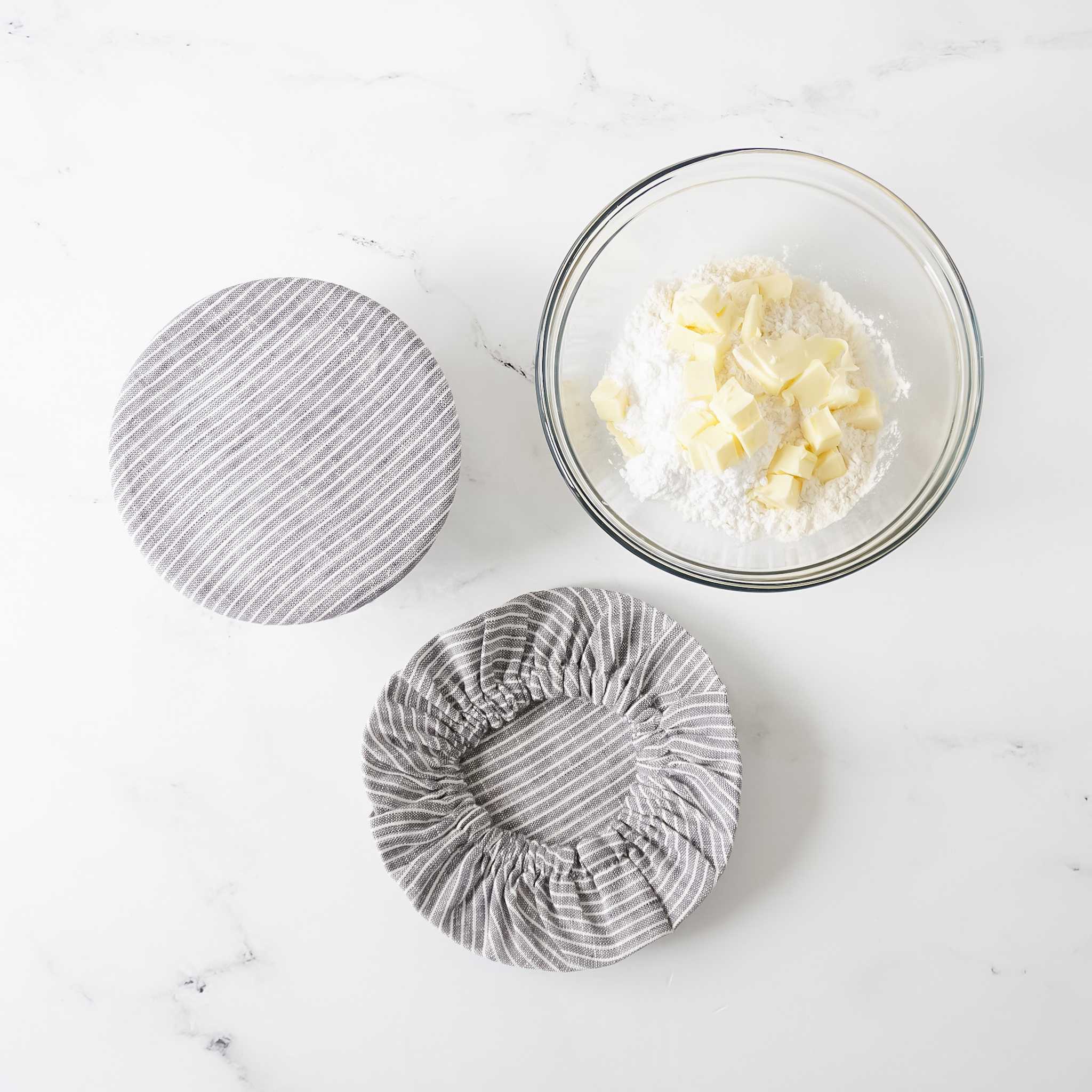 Three bowl covers made of linen, displayed next to a bowl filled with food. The covers are striped in gray and white colors, and come in different sizes.