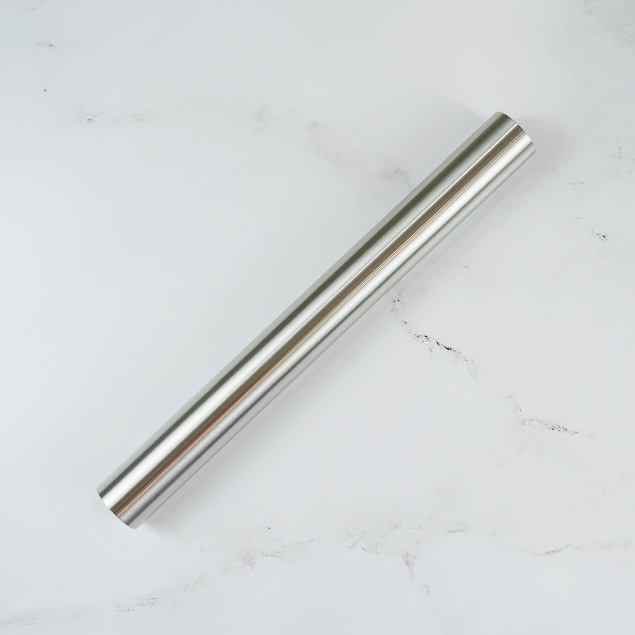 A stainless steel metal rolling pin on a white marble surface.