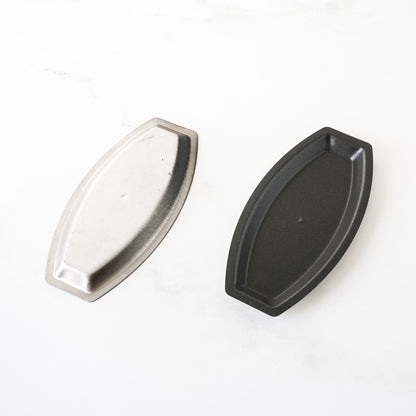 Two salted butter roll pans, one silver and one black, on a white background