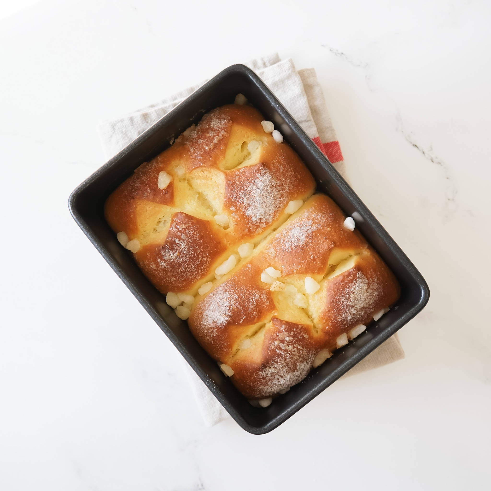 A loaf of brioche bread with a golden brown crust, topped with sugar crystals and dusted with powdered sugar. The bread is sitting on a black wire rack.
