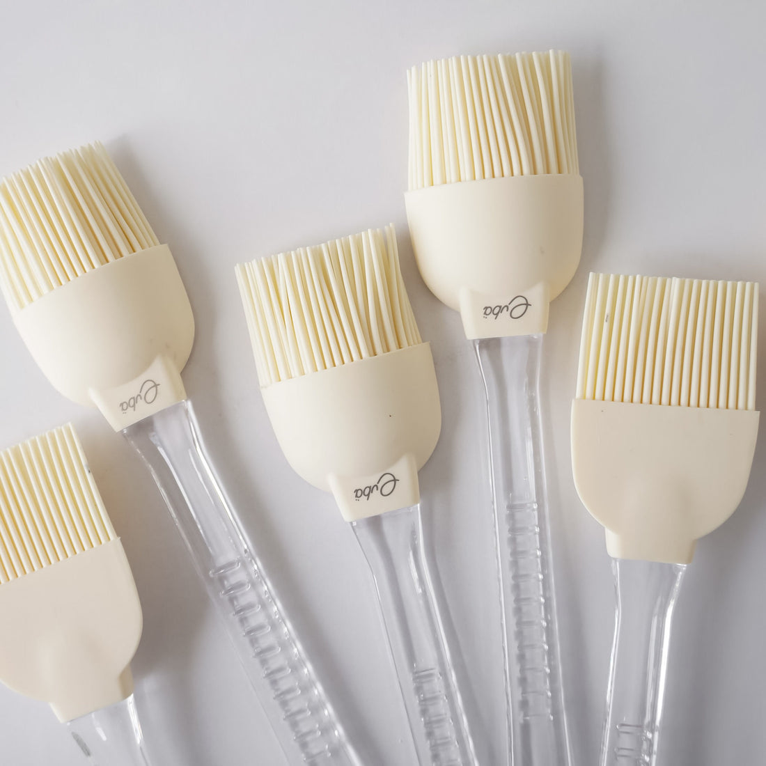 Set of five silicone basting brushes with clear handles on a white background