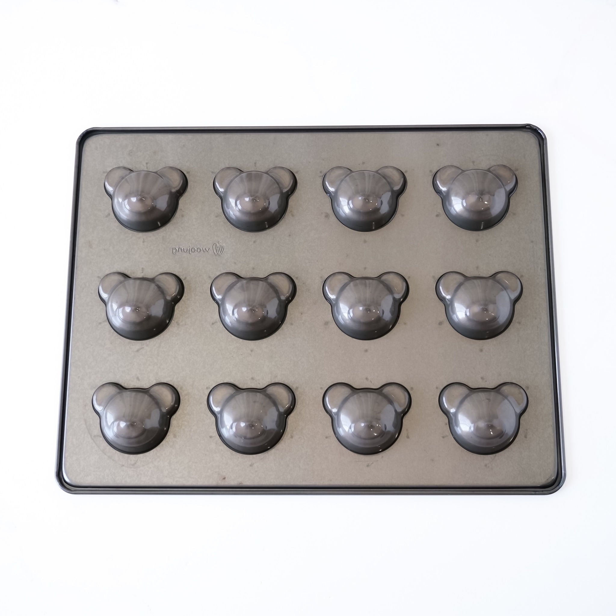 A rectangular metal baking pan with twelve bear-shaped cavities, photographed from above on a plain white background.