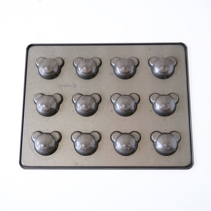 A rectangular metal baking pan with twelve bear-shaped cavities, photographed from above on a plain white background.