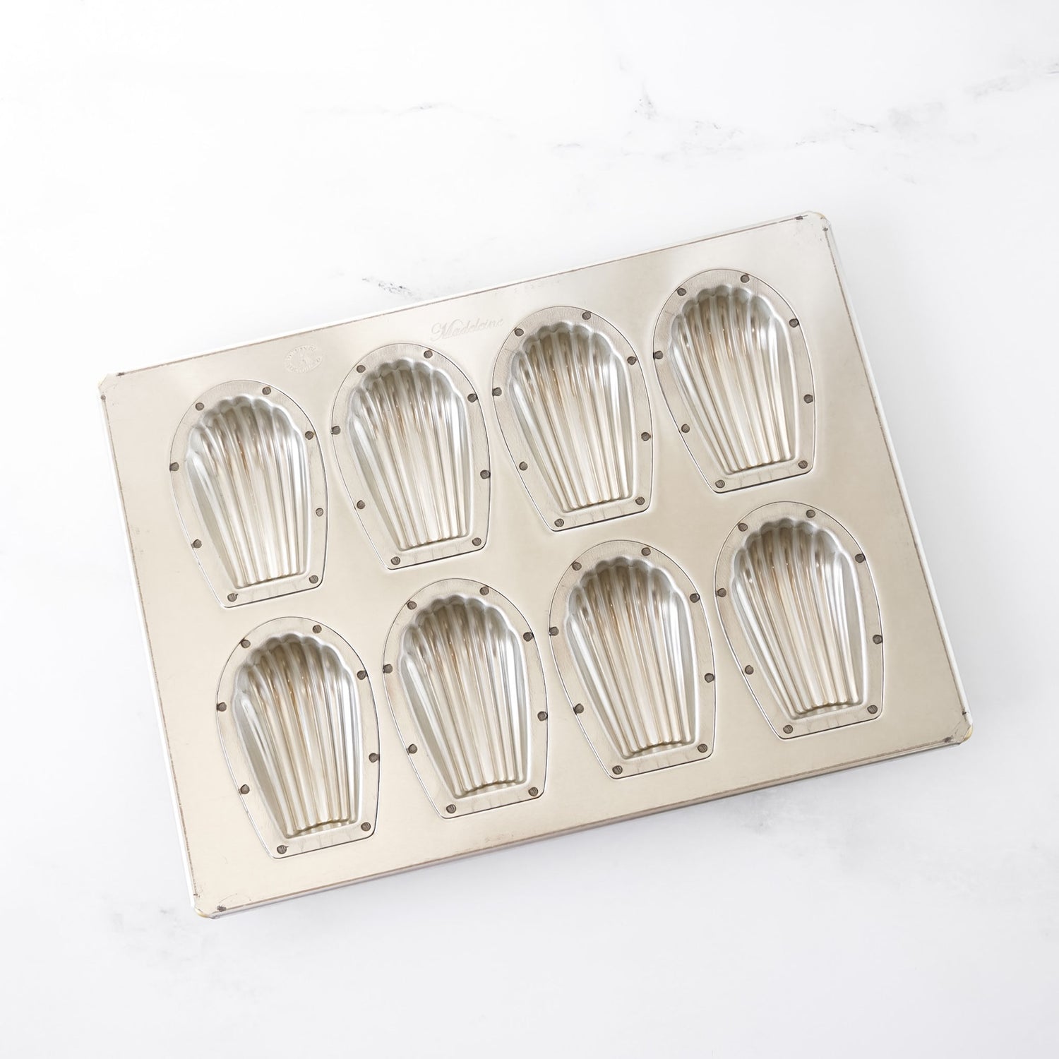 Metallic madeleine mold with eight compartments on a white background