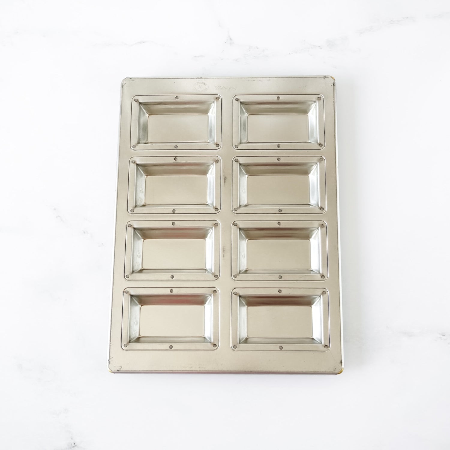 Silicone-coated metallic financier pan with eight square compartments on a white background